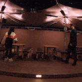 a man and a woman are standing in a room with tables and benches under an umbrella