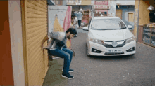 a man sits on a bench in front of a white car with the license plate ts 11 av 111