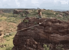 a man is standing on a rope on top of a rocky cliff with the letters th visible in the background