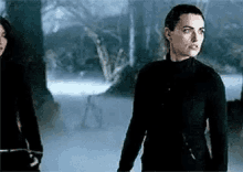 two women in black suits are standing next to each other in a dark forest .