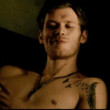 a shirtless man with a tattoo on his chest and a necklace on his neck .