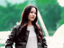 a woman wearing a black leather jacket and a white t-shirt is standing in front of a building .