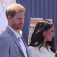 a man in a suit and a woman in a white shirt are standing next to each other and looking at the camera .