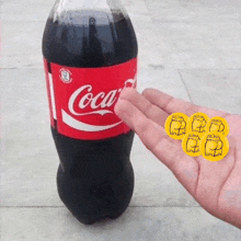 a person is holding a bottle of coca cola next to a bottle of coca cola with stickers on it .