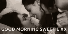 a black and white photo of two women kissing each other on a bed .