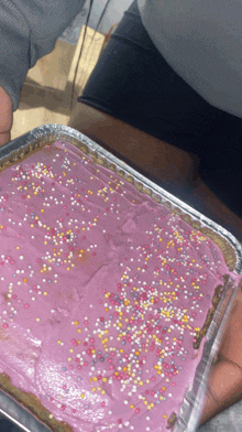 a person is holding a tray of pink cake with sprinkles