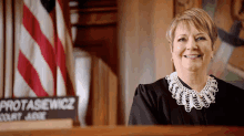 a woman in a judge 's uniform is smiling in front of a sign that says potasiewicz court judge