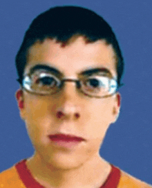 a young man wearing glasses looks at the camera with a blue background