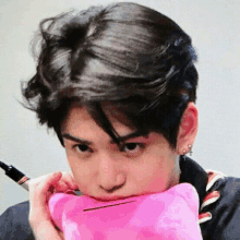 a young man is holding a pink pillow in his mouth and making a funny face .