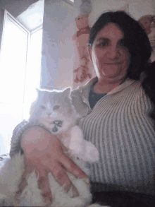 a woman in a sweater holds a white cat with a tag on it that says ' a '