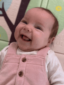 a baby in a pink overalls is smiling and looking up