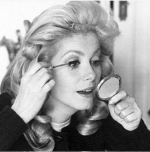 a woman is applying mascara to her eye while looking at herself in a mirror