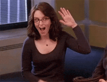 a woman wearing glasses is sitting at a table and waving her hand .