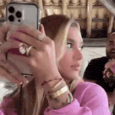 a woman in a pink sweater is taking a selfie with her cell phone .