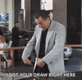a man in a suit says " i got your draw right here " in a car dealership