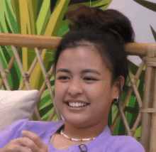 a woman in a purple shirt is smiling while sitting in a wicker chair