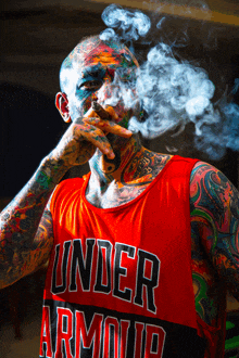 a man with a lot of tattoos is wearing a red under armour tank top