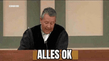 a judge is sitting at a table with a sign that says alles ok .