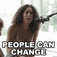 a woman is sitting in front of a microphone with the words `` people can change '' written on it .