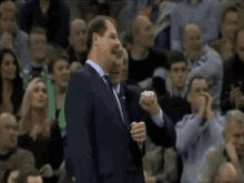 a man in a suit and tie is giving a thumbs up in front of a crowd at a basketball game .