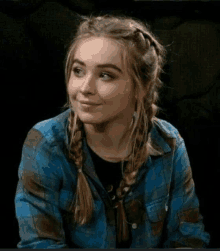 the girl is wearing a plaid shirt and braids and smiling .