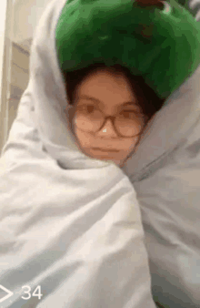 a woman wearing glasses is wrapped in a blanket with a stuffed frog on her head .