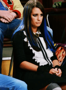 a woman with blue hair sits in a chair with other people