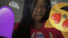 a woman wearing glasses and a red shirt is holding a purple heart and a yellow emoji with hearts on it