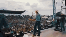 a man in a cowboy hat is playing a guitar on stage in front of a crowd of people .