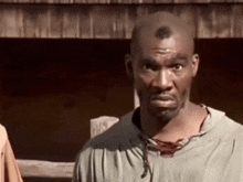 a man with a shaved head is standing in front of a wooden fence .