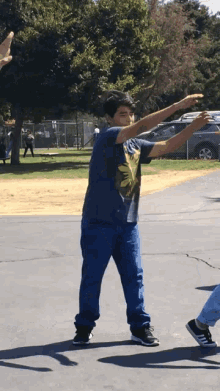 a boy wearing a blue shirt with a yellow leaf on it is standing in a park with his arms outstretched