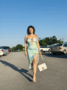 a woman in a dress is walking in a parking lot with a white purse