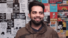 a man with a beard is smiling in front of a wall covered in posters including one that says " live your own life "