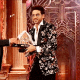 a man in a floral suit is holding a trophy that says dd