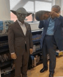 a man in a suit is standing next to a yoda statue .