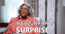a woman in a floral shirt is sitting in a chair with the words `` hellurrr surprise '' written on the screen .