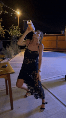 a woman in a black dress is drinking from a bottle at night