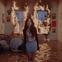 a woman in a plaid skirt is standing in front of a room on fire .