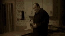 a man in a black coat is standing in a kitchen holding a bottle of alcohol .