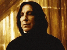 a man with long hair is standing in front of a window looking at the camera .