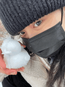 a woman wearing a black mask is holding a snowball in her hand