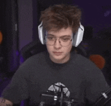 a young man wearing headphones and glasses is sitting in front of a microphone in a dark room .