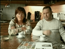 a man and a woman are sitting at a table in a kitchen with sbs written on the bottom of the screen .