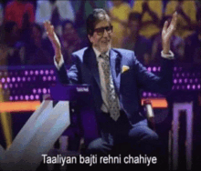 a man in a suit and tie is sitting in front of a crowd with the words taaliyan bajti rehni chahiye on the bottom