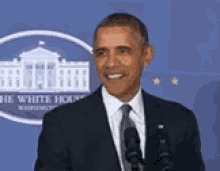 a man in a suit and tie is standing in front of two microphones in front of the white house .