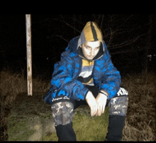 a man in a blue jacket sits on a rock with his hands on his knees