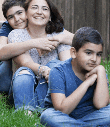 a woman sits in the grass with two boys hugging her