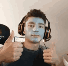 a man with blue paint on his face and headphones is giving two thumbs up .