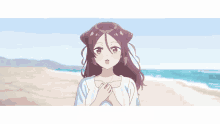 a girl is standing on a beach with her hands on her chest and looking at the camera .