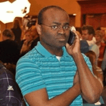 a man wearing glasses and a blue shirt is talking on a cell phone